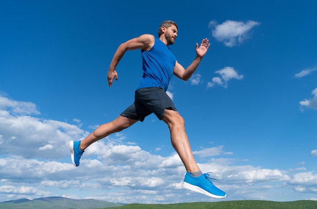 Velocista sportivo con corpo muscoloso che corre in abbigliamento sportivo all'aperto sulla resistenza del fondo del cielo