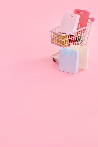 Vendita annuale stagione dello shopping concetto mini carrello rosa carrello carrello pieno di sacchetto di carta regalo isolato su sfondo rosa pallido spazio vuoto copia primo piano