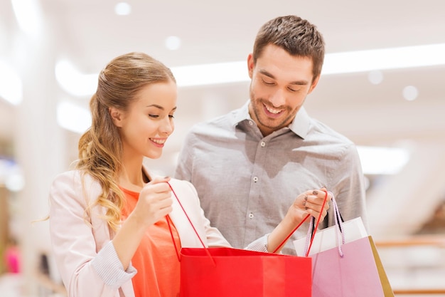 vendita, consumismo e concetto di persone - giovane coppia felice che mostra il contenuto delle borse della spesa nel centro commerciale