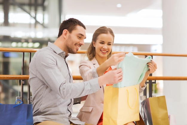 vendita, consumismo e concetto di persone - giovane coppia felice che mostra il contenuto delle borse della spesa nel centro commerciale