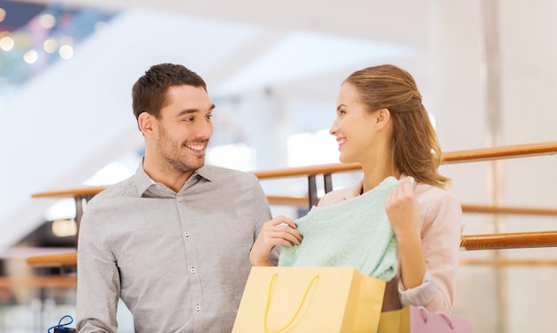 vendita, consumismo e concetto di persone - giovane coppia felice che mostra il contenuto delle borse della spesa nel centro commerciale