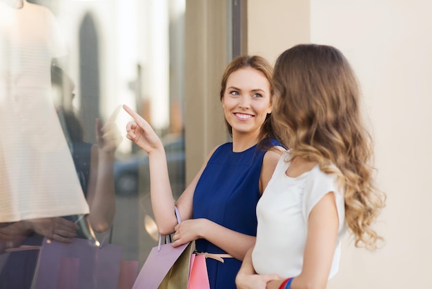 vendita, consumismo e concetto di persone - giovani donne felici con borse della spesa che puntano il dito verso la vetrina in città