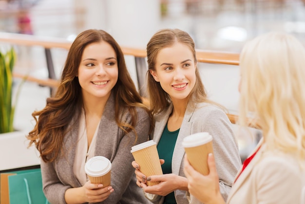 vendita, consumismo e concetto di persone - giovani donne felici con borse della spesa e bicchieri di carta da caffè nel centro commerciale