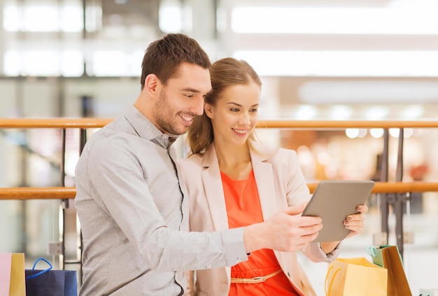 vendita, consumismo, tecnologia e concetto di persone - giovane coppia felice con borse della spesa e computer tablet pc nel centro commerciale