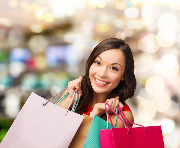 vendita, regali, natale, concetto di natale - donna sorridente in vestito rosso con le borse della spesa