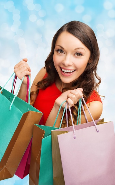 vendita, regali, natale, vacanze e concetto di persone - donna sorridente con borse della spesa colorate su sfondo di luci blu