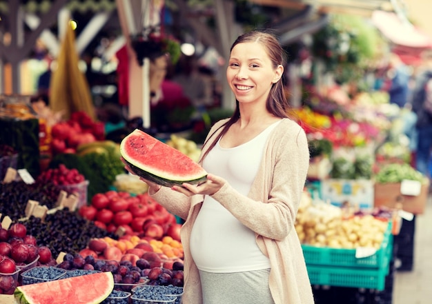 vendita, shopping, cibo, gravidanza e concetto di persone - donna incinta felice che sceglie l'anguria al mercato di strada