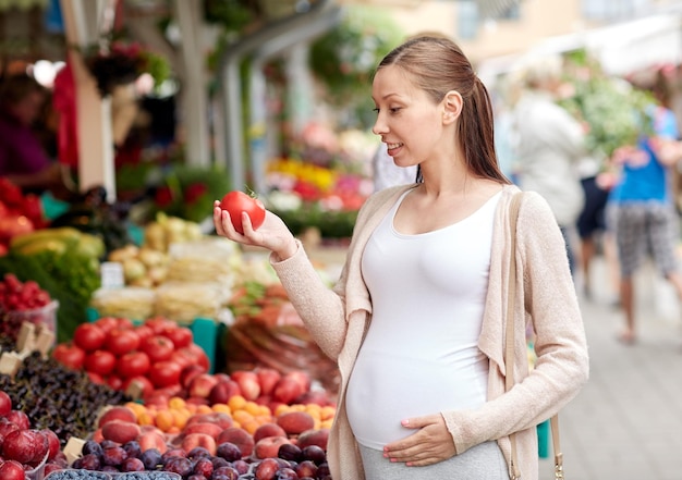 vendita, shopping, cibo, gravidanza e concetto di persone - donna incinta felice che tiene pomodoro al mercato di strada