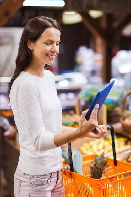 vendita, shopping, consumismo e concetto di persone - giovane donna felice con cesto di cibo e computer tablet pc nel mercato