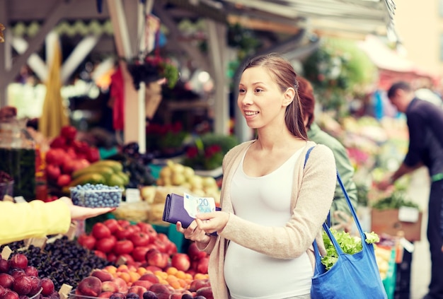 vendita, shopping, gravidanza e concetto di persone - donna incinta felice con portafoglio e soldi che comprano cibo al mercato di strada