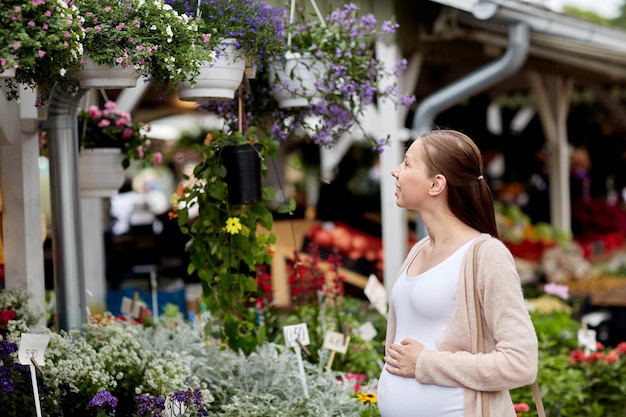 vendita, shopping, gravidanza, giardinaggio e concetto di persone - donna incinta felice che sceglie i fiori al mercato di strada