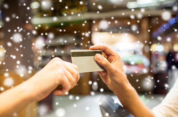 vendita, shopping, pagamento, consumismo e concetto di persone - primo piano delle mani che danno carta di credito alla cassa nel mercato o nel centro commerciale sull'effetto neve