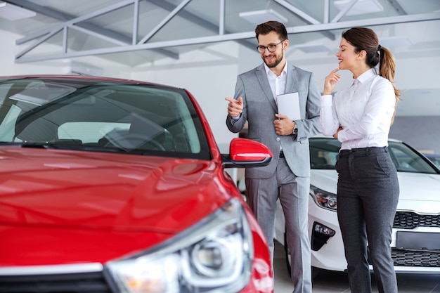 Venditore di auto che tiene tablet e parla delle specifiche e delle prestazioni dell'auto a una donna che vuole acquistare una nuova auto.