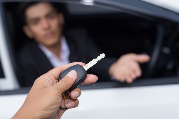 Venditore di auto consegna la chiave per una nuova auto a un giovane uomo d&#39;affari di fronte alla macchina bianca