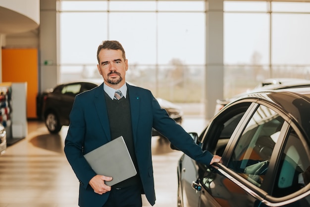 Venditore di auto in piedi accanto a una macchina in showroom.