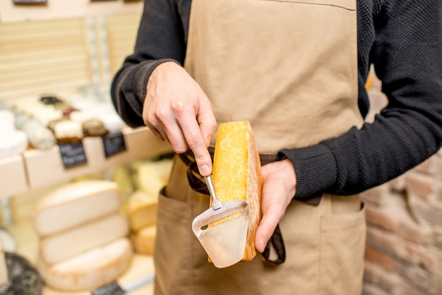 Venditore di formaggio in uniforme che taglia formaggio stagionato con affettatrice nel negozio
