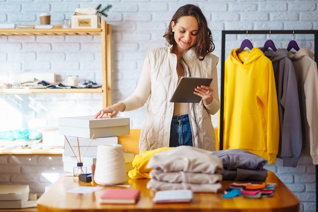 Venditore di imprenditore proprietario di piccola impresa che utilizza tablet che controlla gli ordini del negozio di abbigliamento e-commerce