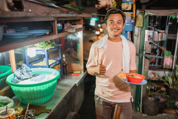 Venditore maschio asiatico che tiene una ciotola di pasta con il gesto del pollice in su