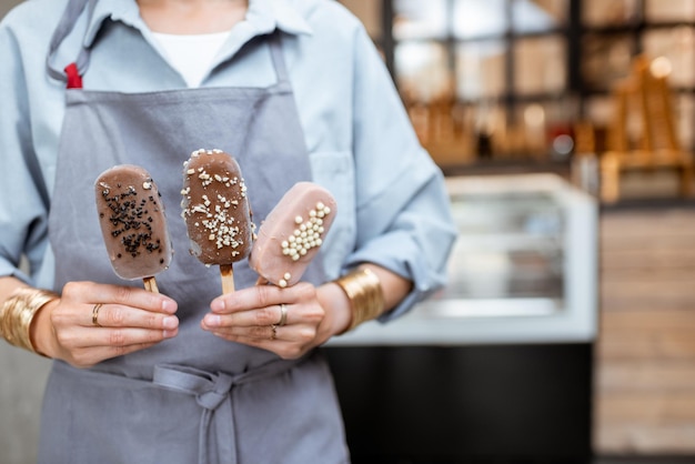 Venditrice che tiene il gelato al cioccolato su un bastone nel negozio in primo piano sulle mani e il gelato