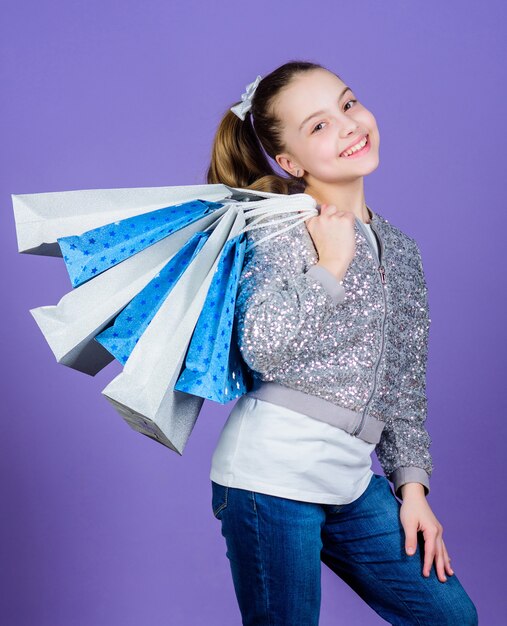 Venerdì nero. Sconto di vendita. Giornata di shopping. Pacchetti del mazzo della stretta del bambino. Moda per bambini. Festeggiata. Marchi preferiti e tendenze più in voga. Ragazza con borse della spesa sfondo viola. Acquisto e acquisto.