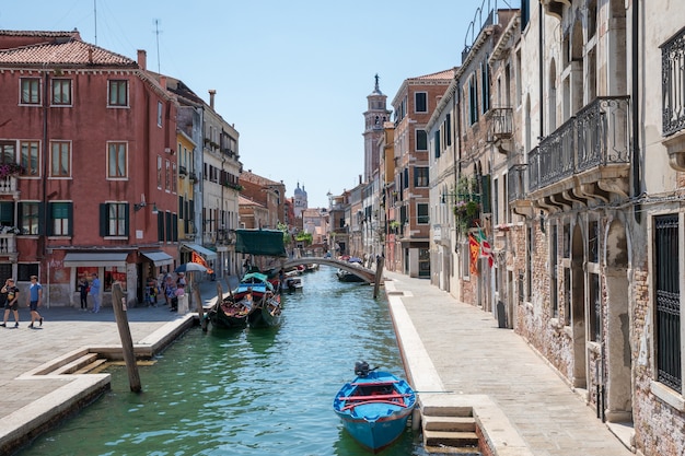 Venezia, Italia - 1° luglio 2018: Vista panoramica dello stretto canale di Venezia con edifici storici e barche dal ponte. Le persone si rilassano e camminano. Paesaggio della giornata di sole estivo