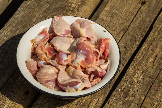 Ventrigli di pollo crudo in ciotola di metallo smaltato su tavola in legno rustico