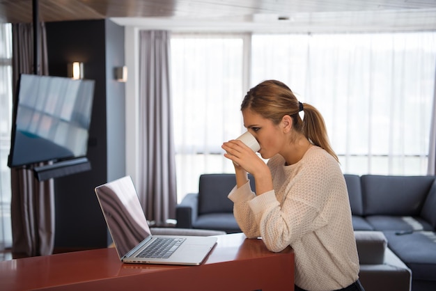 Vera donna che usa il computer portatile a casa a bere caffè godendosi il relax