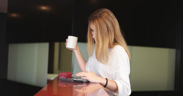 Vera donna che utilizza il telefono cellulare a casa bevendo caffè godendosi il relax