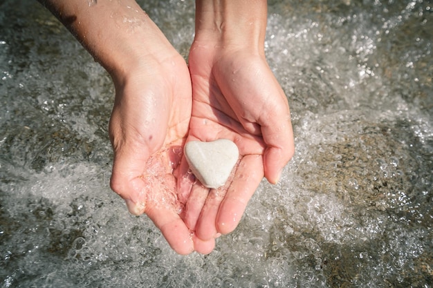 Vera pietra di mare naturale a forma di cuore nelle mani delle donne lavate dall'acqua di mare