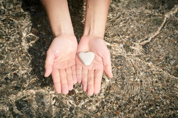 Vera pietra di mare naturale a forma di cuore nelle mani delle donne lavate dall'acqua di mare