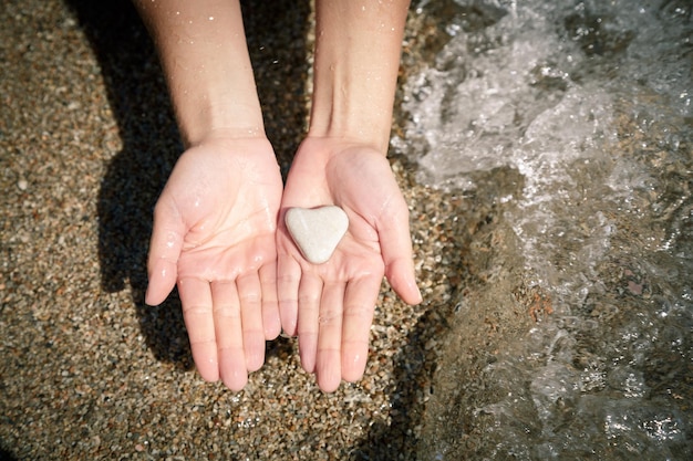 Vera pietra di mare naturale a forma di cuore nelle mani delle donne lavate dall'acqua di mare