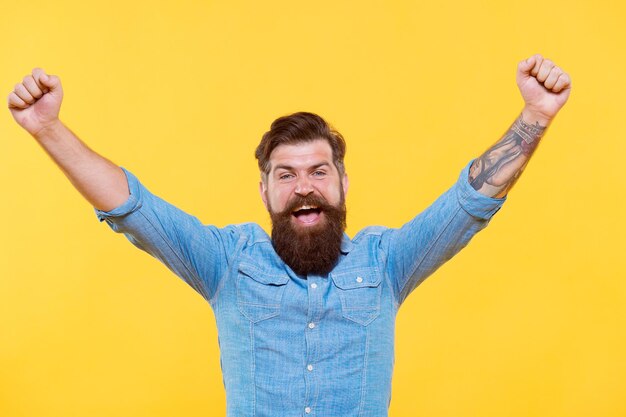 Vera vittoria non facile da ottenere nella vita. Felice hipster con le mani alzate sfondo giallo. L'uomo barbuto celebra la vittoria. Godendo la vittoria. Vittoria o successo. È campione.