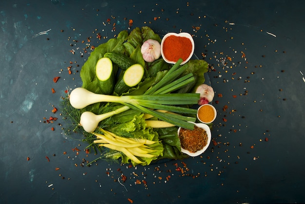 VERDURE A BORDO DI LEGNO SU UNA PIETRA. GIOVANI CIPOLLE DI ERBE FAGIOLI VERDI ALL'AGLIO GIALLO DI MAIS ZUCCHINI SPEZIE LUMINOSE SI TROVANO SU UNA TAVOLA DI LEGNO SCURO SU UNA STRUTTURA STRUTTURATA.