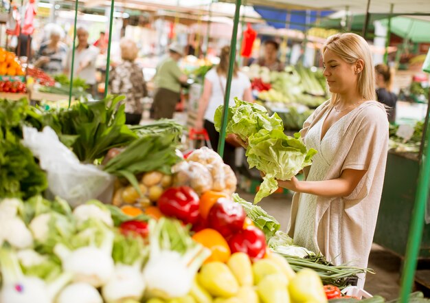 Verdure d&#39;acquisto della giovane donna sveglia al mercato