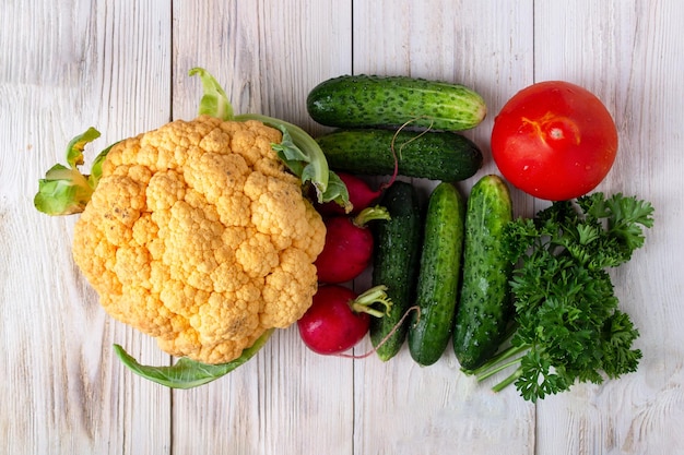 Verdure dal giardino cavolfiore giallo cetrioli pomodori ravanelli prezzemolo su uno sfondo bianco