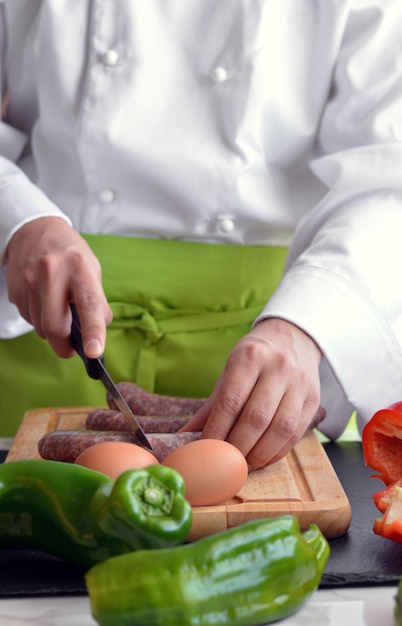 Verdure di taglio del cuoco unico al tavolo per cucinare