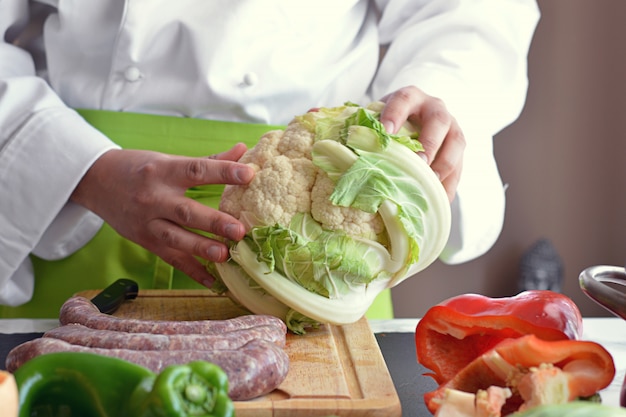 Verdure di taglio del cuoco unico al tavolo per cucinare