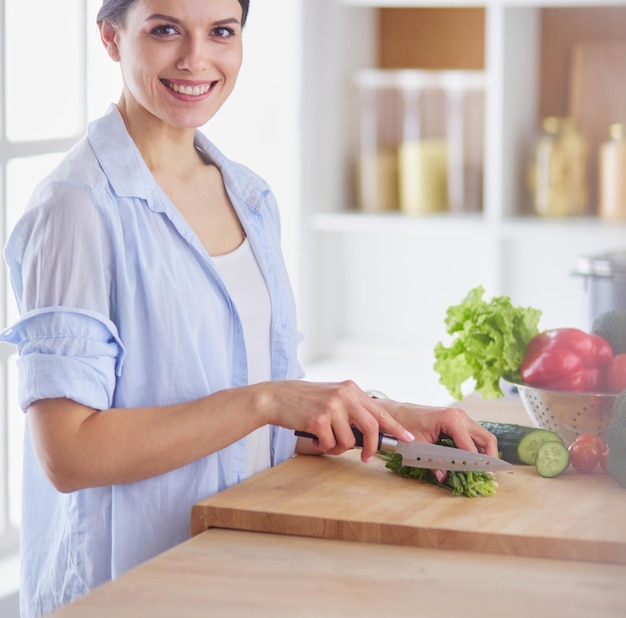 Verdure di taglio della giovane donna in cucina a casa.