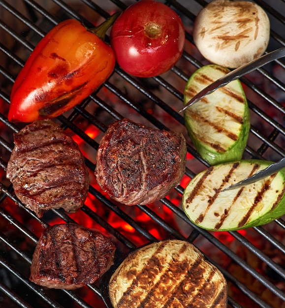 Verdure e carne sfrigolante alla griglia con fiamme, primi piani