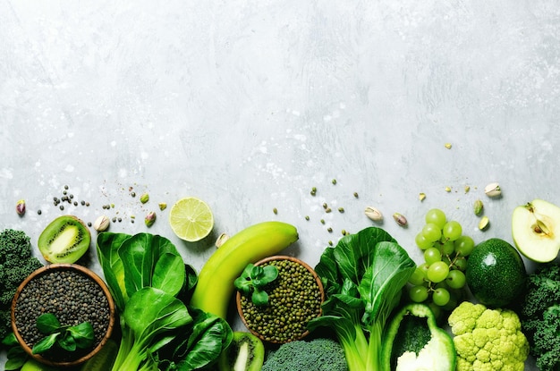 Verdure e frutta verdi biologiche su sfondo grigio Copia spazio piatto vista dall'alto Mela verde zucchine cetriolo avocado cavolo lime kiwi uva banana broccoli lenticchie marmorizzate fagiolo mung