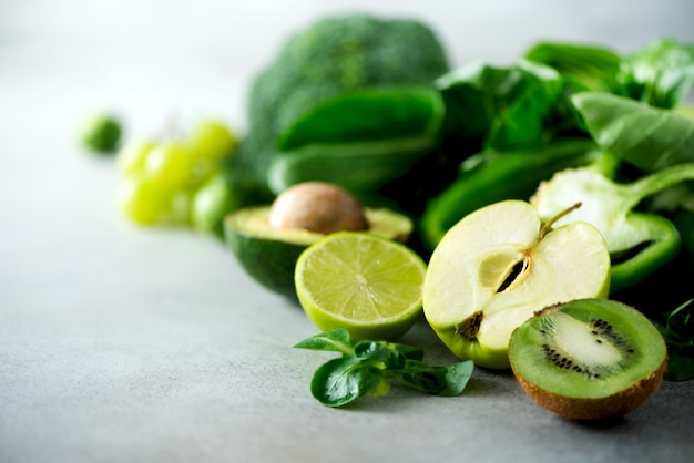 Verdure e frutta verdi organiche su fondo grigio. Mela verde, lattuga, cetriolo, avocado, cavolo, lime, kiwi, uva, banana, broccoli
