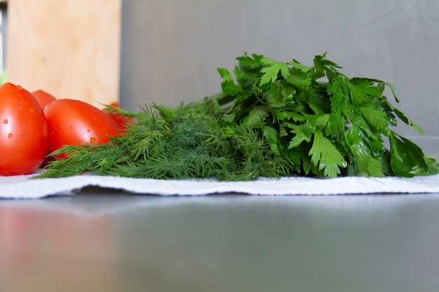 Verdure fresche cetrioli pomodori e verdure con aneto e prezzemolo giacciono sulla superficie grigia della cucina su un asciugamano di lino