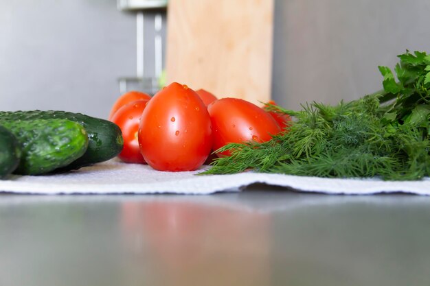 Verdure fresche cetrioli pomodori e verdure con aneto e prezzemolo giacciono sulla superficie grigia della cucina su un asciugamano di lino