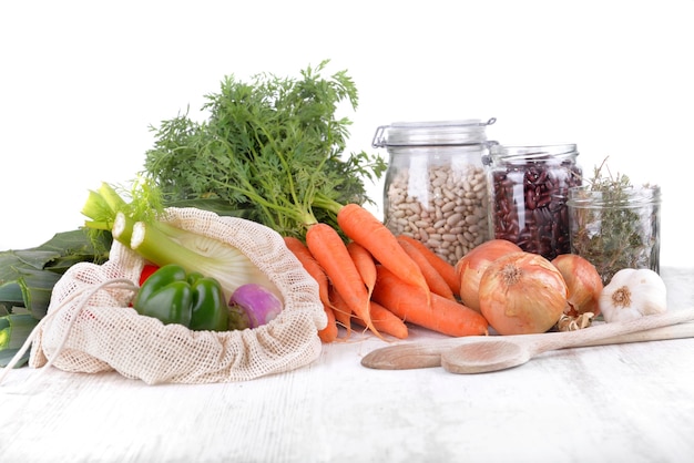 Verdure fresche in un sacchetto riutilizzabile e fagioli secchi in vaso con cipolle e aglio su un tavolo