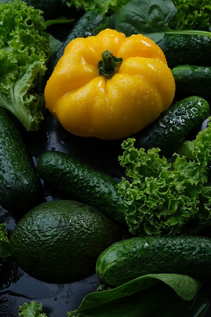 Verdure fresche, peperoni gialli, cetrioli e insalata su sfondo nero.