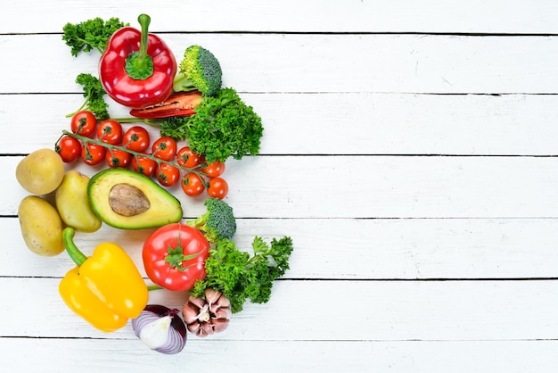 Verdure fresche su uno sfondo di legno bianco Avocado pomodori aglio prezzemolo paprika Vista dall'alto Spazio libero per il testo