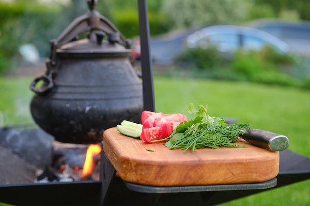 Verdure fresche sul tagliere e pentola di ghisa sul fuoco sullo sfondo