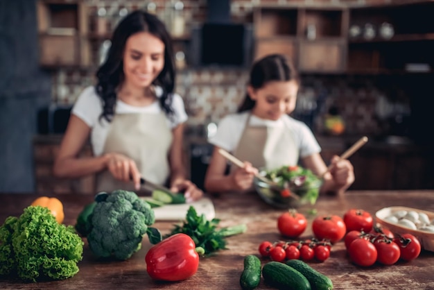 Verdure fresche sul tavolo con la figlia e la madre che preparano insieme insalata fresca sullo sfondo