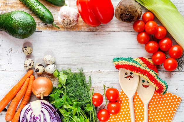 Verdure fresche sulla tavola di legno con cucchiai divertenti con facce e cappelli estivi