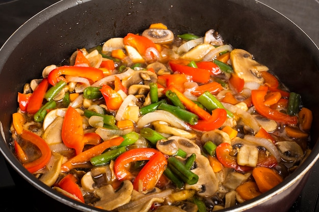 Verdure fritte con funghi in padella su uno sfondo scuro. Cucinare il cibo